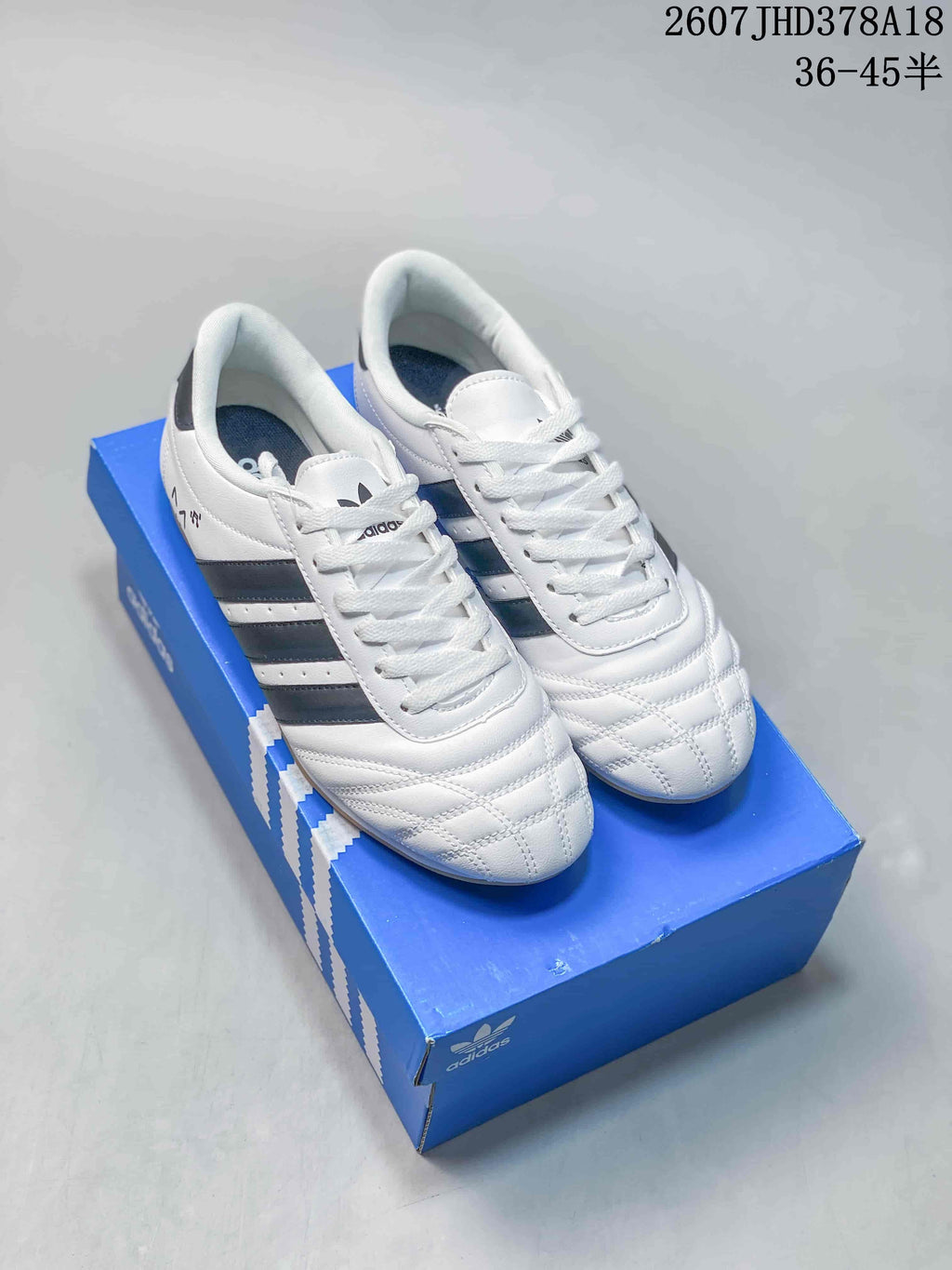Pair of white adidas sneakers with dark side stripes and quilted forefoot panels displayed on a blue shoebox.