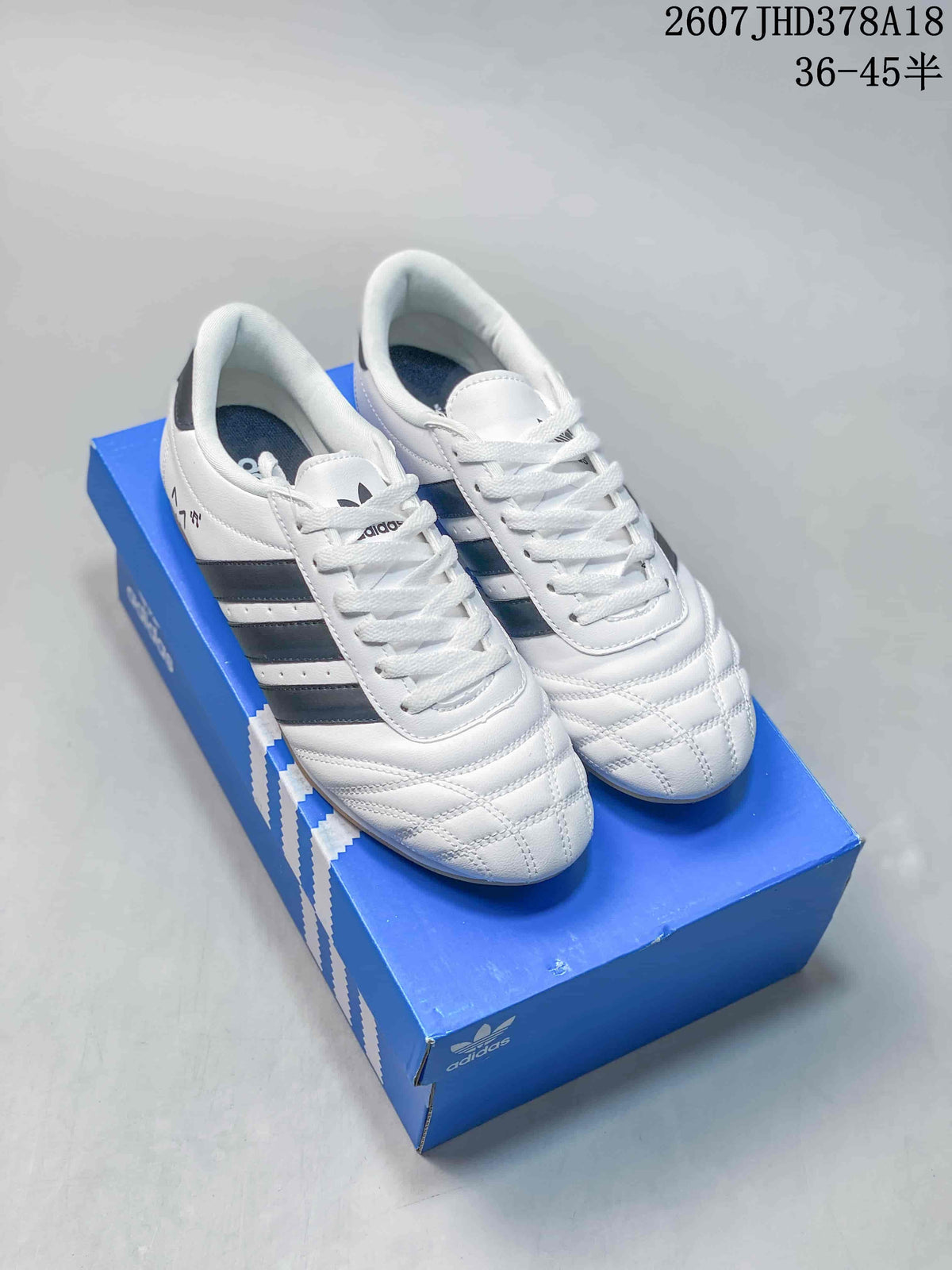 Pair of white adidas sneakers with dark side stripes and quilted forefoot panels displayed on a blue shoebox.