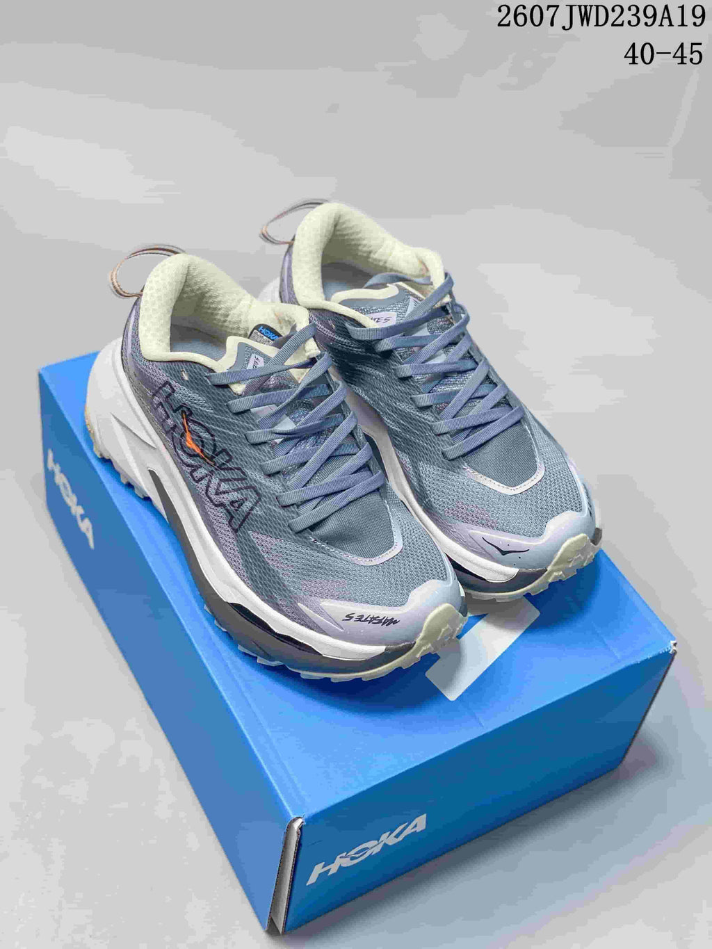 Pair of gray HOKA Rocket X 3 shoes displayed on a blue shoebox, showing the lace-up upper and sculpted sole.
