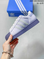 Side profile of a lavender Adidas Superstar sneaker showing the decorative three-stripe area and shell toe.