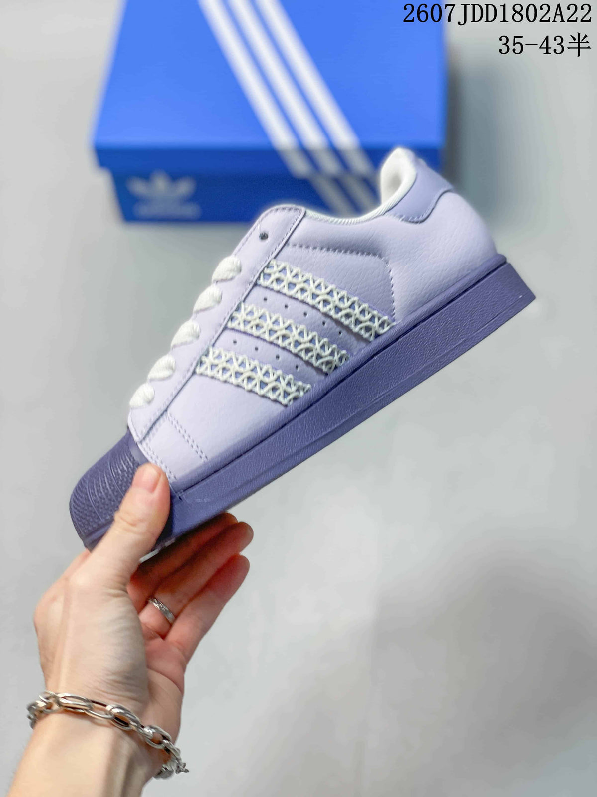 Side profile of a lavender Adidas Superstar sneaker showing the decorative three-stripe area and shell toe.