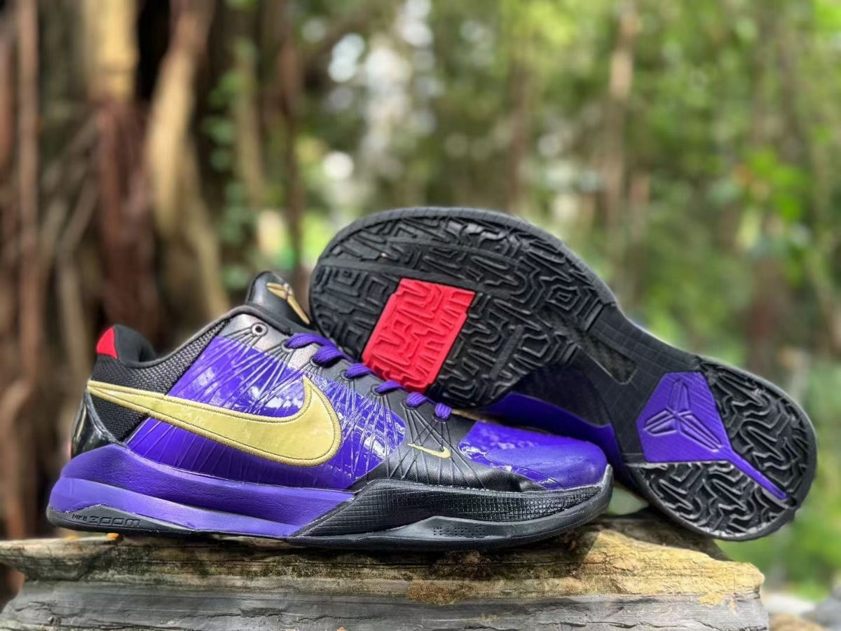 Nike Kobe 5 basketball shoes in purple, black and gold, shown from the side with the outsole visible.