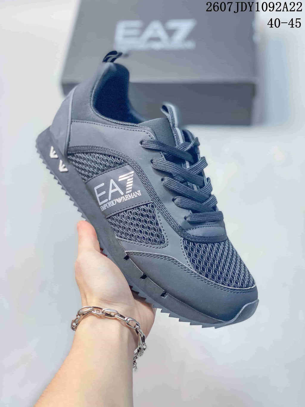 Close-up of a dark gray EA7 sneaker showing the side logo panel, textured mesh-style inserts and lace-up construction.