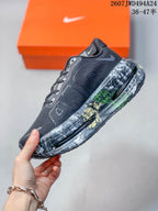 Side view of a black and gray sneaker showing the lace-up upper, Nike branding, and visible midsole cushioning windows.