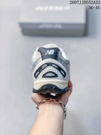 Rear view of a white and silver sneaker showing the New Balance tongue branding, layered heel panels, and black outsole.
