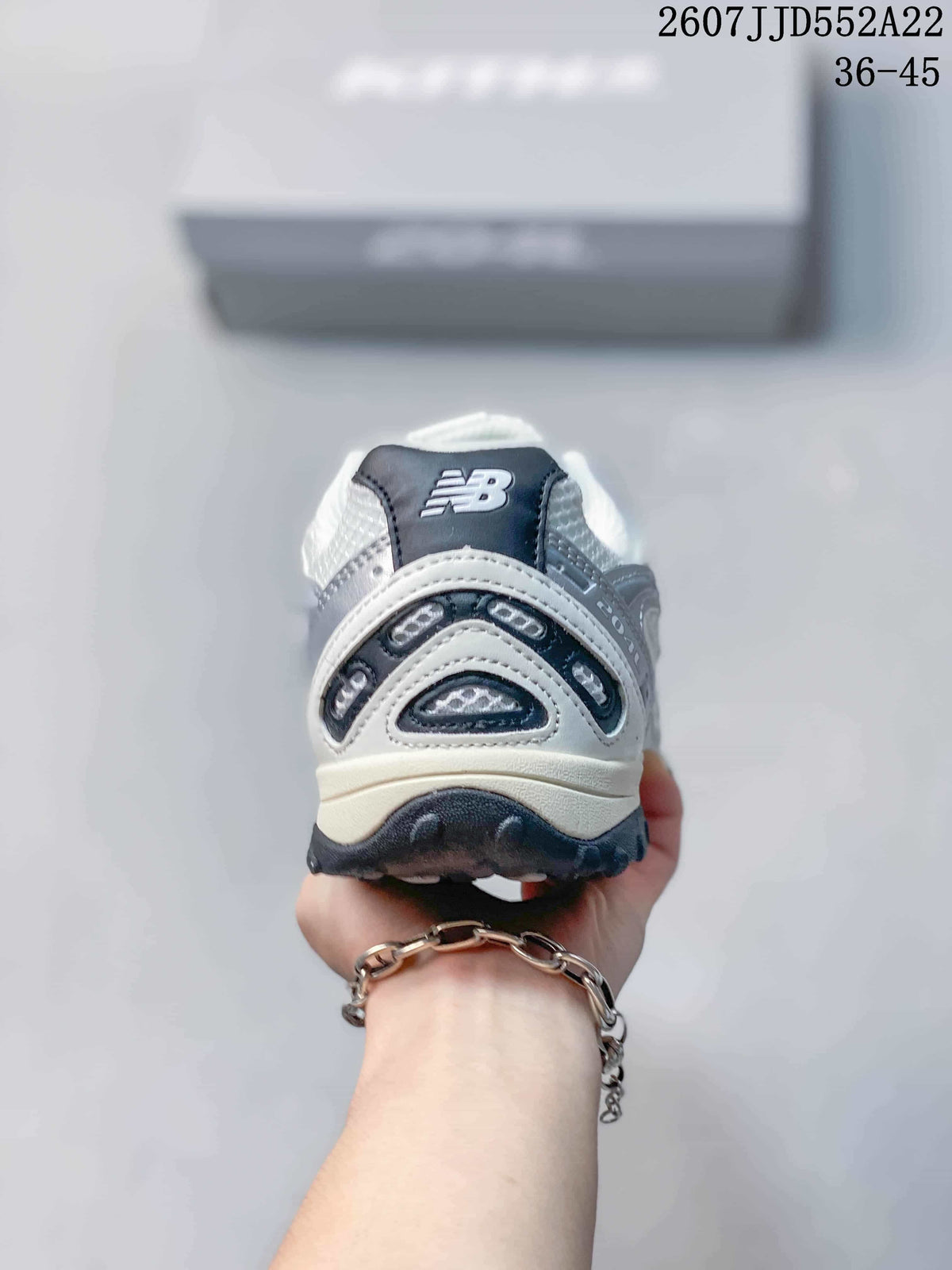 Rear view of a white and silver sneaker showing the New Balance tongue branding, layered heel panels, and black outsole.