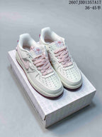 Pair of white Nike low-top sneakers with pink laces, blue details and mauve outsoles displayed on a heart-patterned box.