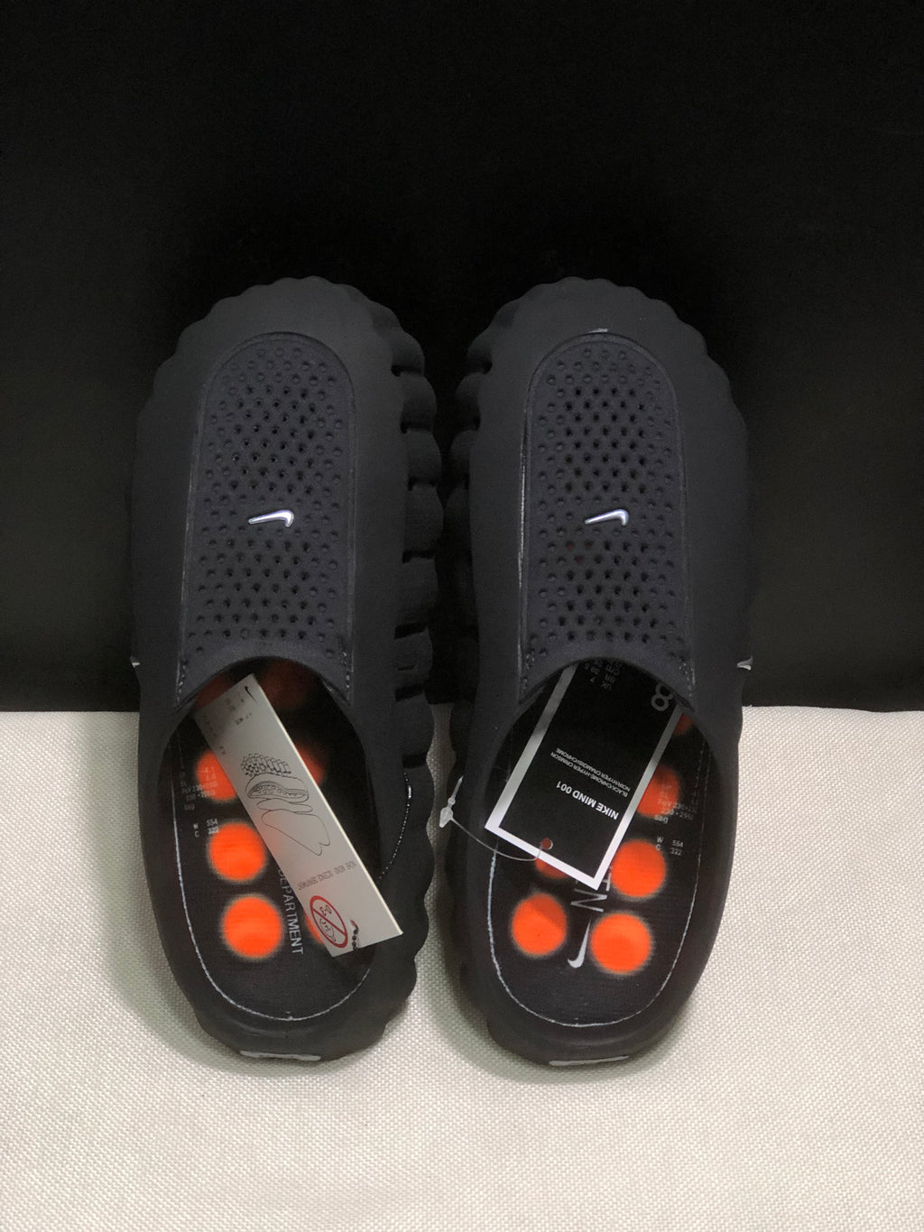 Top view of the black slides showing textured footbeds, orange circular outsole elements, and product inserts.