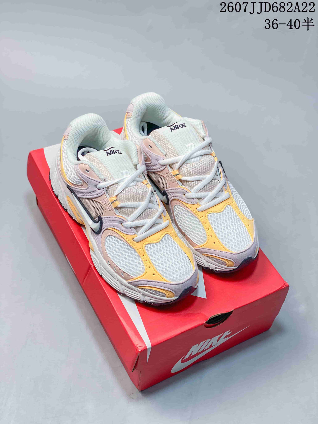 Pair of Nike V5 RNR sneakers in pink, yellow, white and gray shown on a red Nike shoebox; image text shows style code 2607JJD682A22 and size range 36–40.