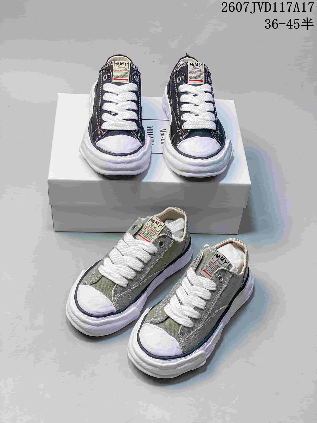 Black and olive MMY low-top canvas sneakers arranged around a shoebox, showing white laces, toe caps and sculpted soles.