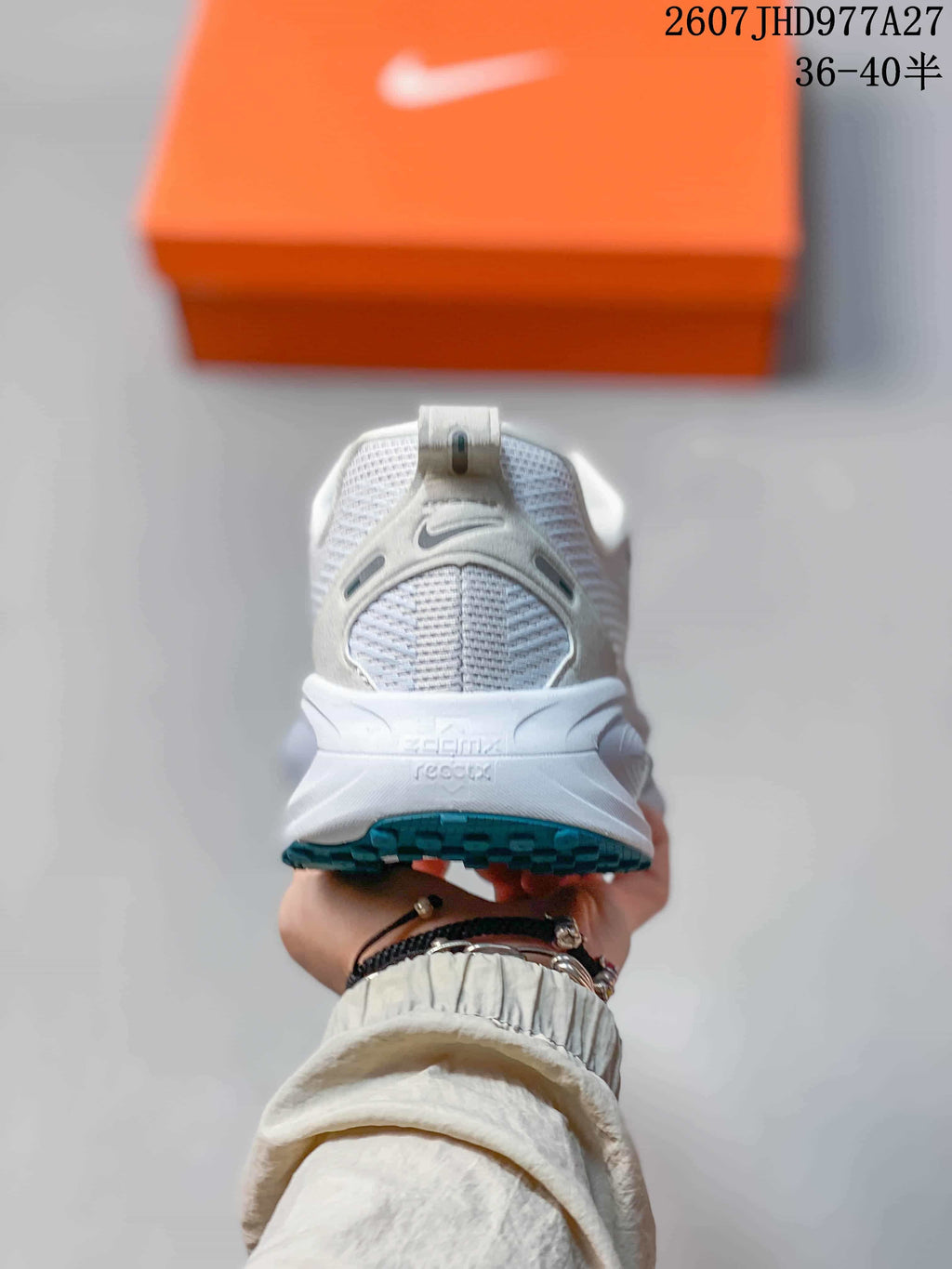 Rear view of a white sneaker showing the padded heel collar, pull tab, heel branding and teal outsole edge; overlay text shows style code 2607JHD977A27 and sizes 36–40.5.