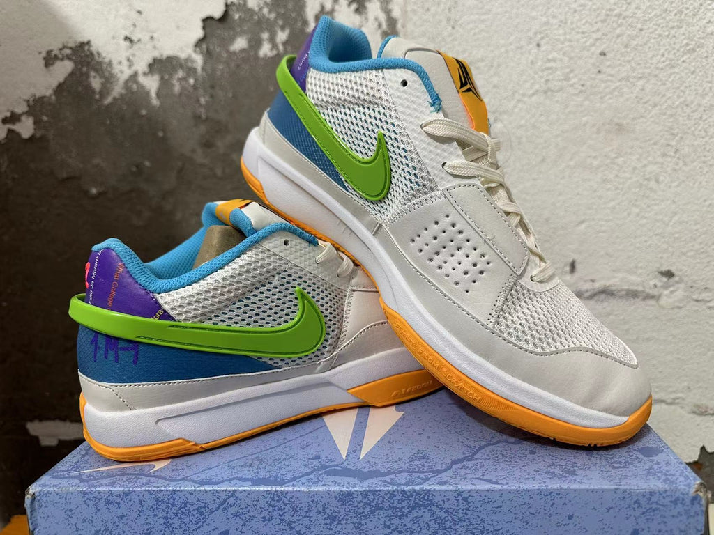 Pair of white Nike Ja 1 shoes shown at an angle with green side logos, blue and purple accents, and orange outsoles