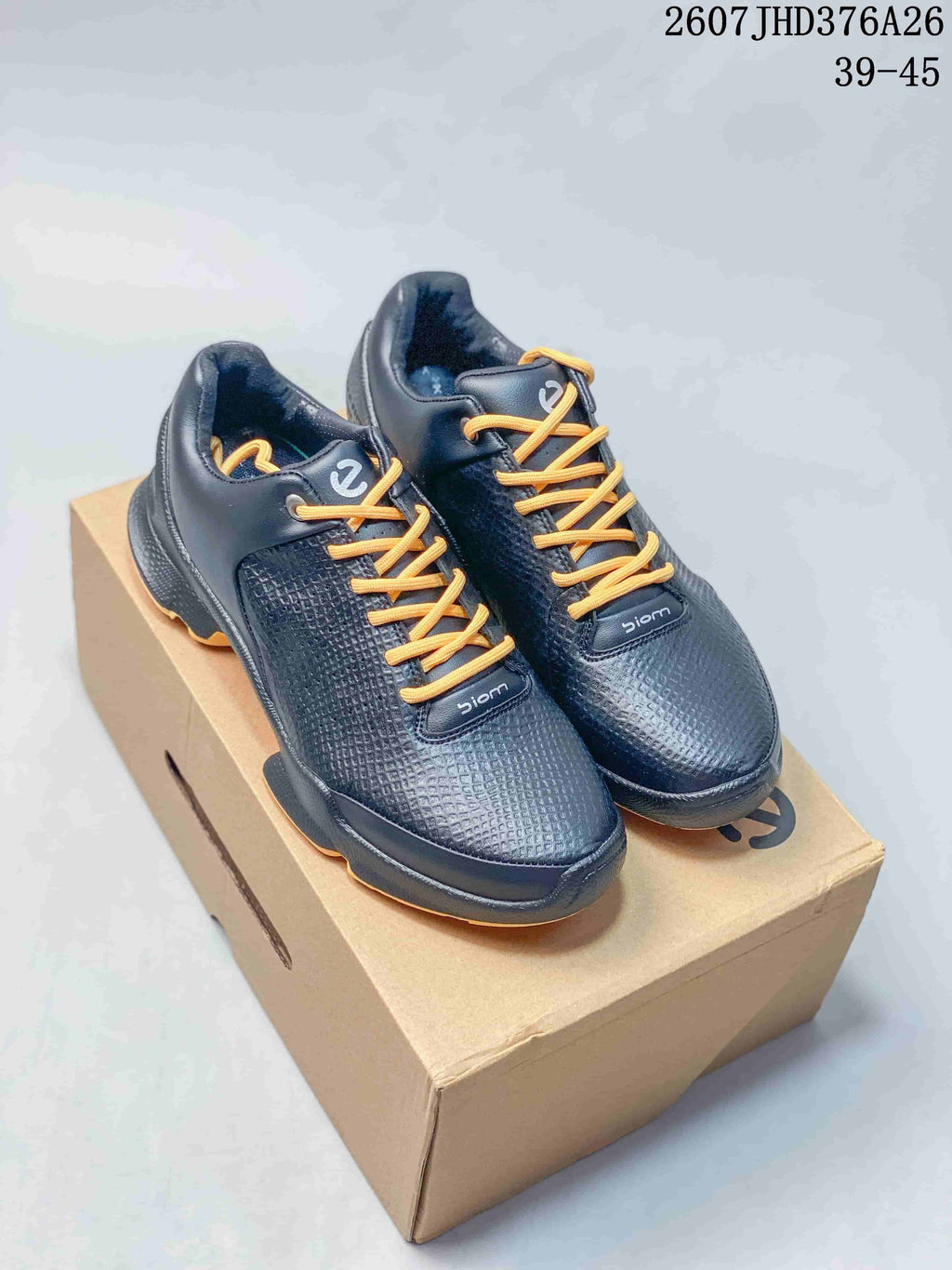 Pair of black ECCO BIOM sneakers with gold laces displayed on a shoebox; image text shows style code 2607JHD376A26 and size range 39–45.