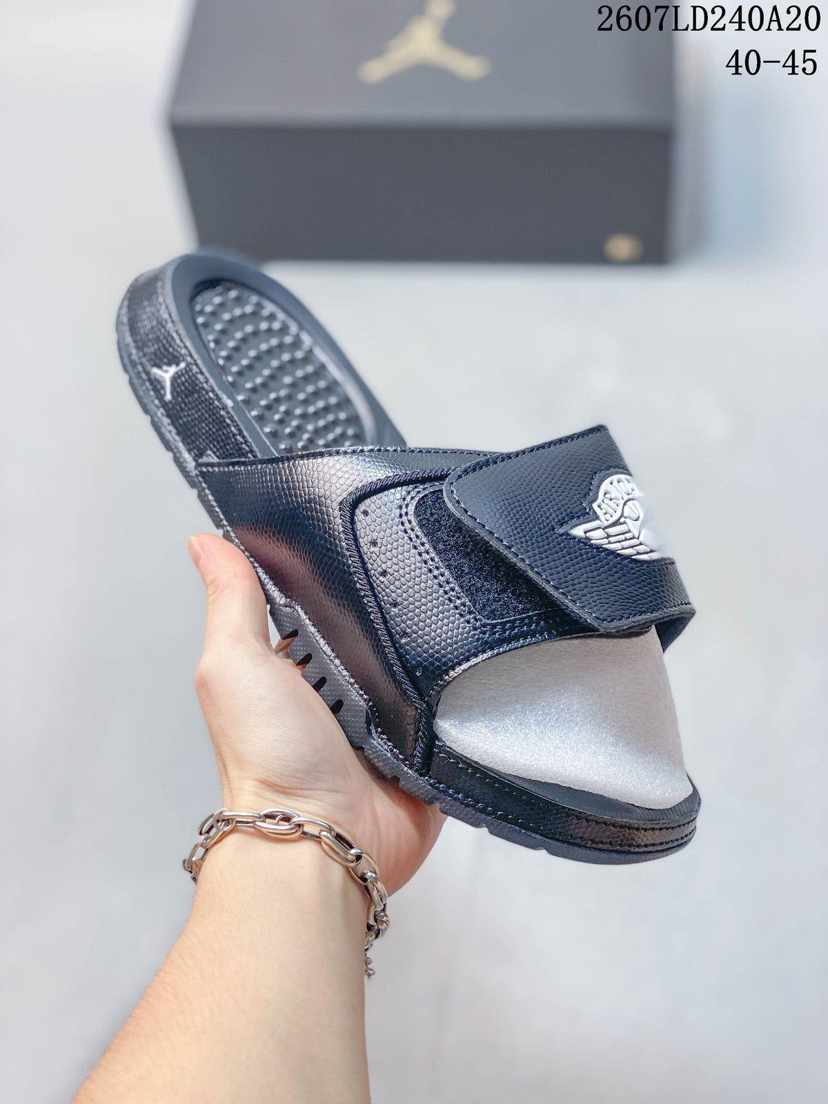 Angled view of a dark Jordan slide showing the adjustable strap, textured footbed, and patterned outsole; style code 2607LD240A20 and size range 40–45 appear above.
