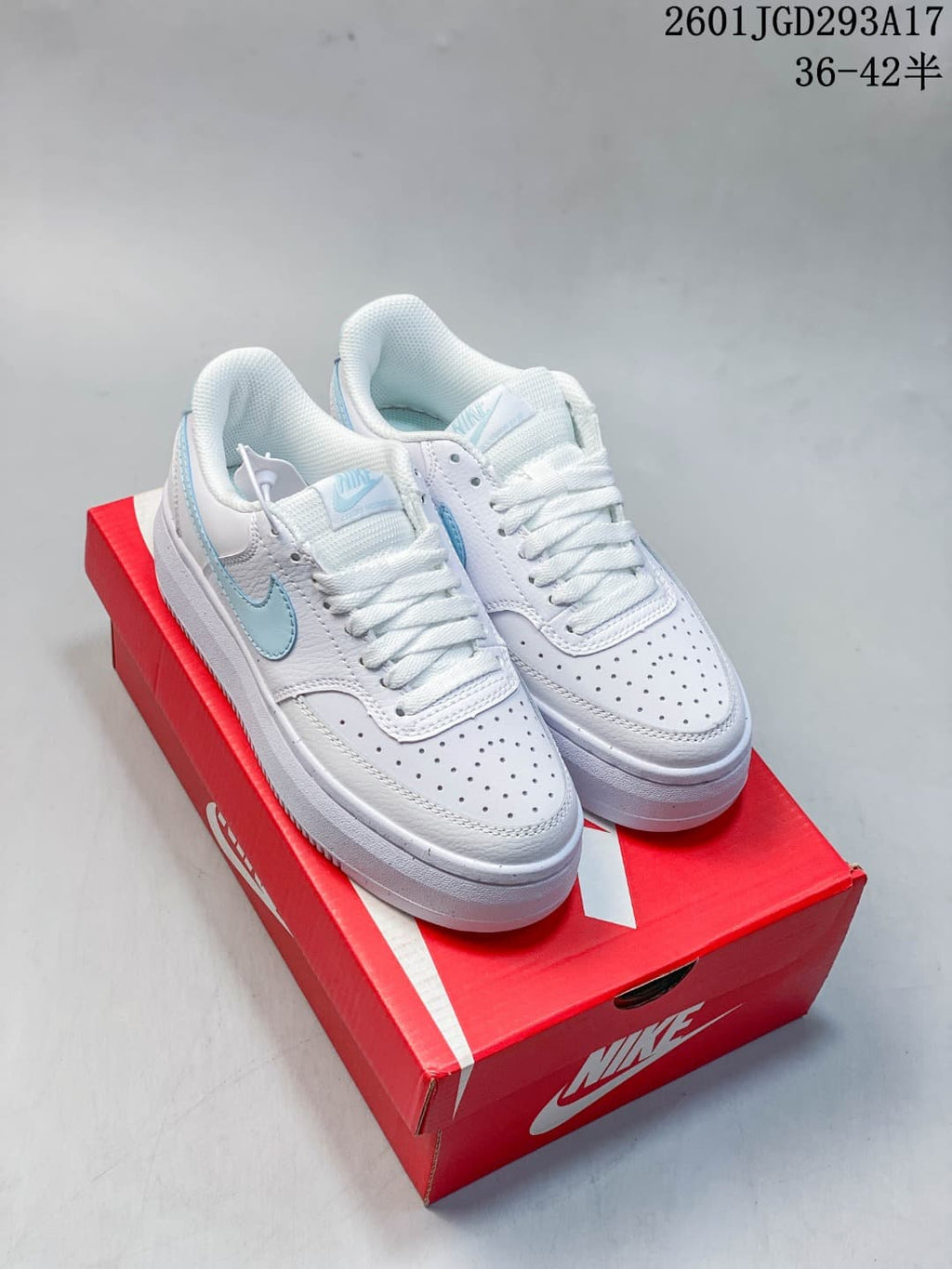 Pair of white and light blue Nike Court Vision Alta sneakers displayed on a red Nike shoe box.