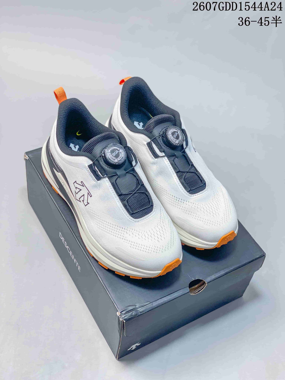 Pair of white Descente low-top sneakers with black panels, orange outsole accents, BOA-style dials, and a shoe box.