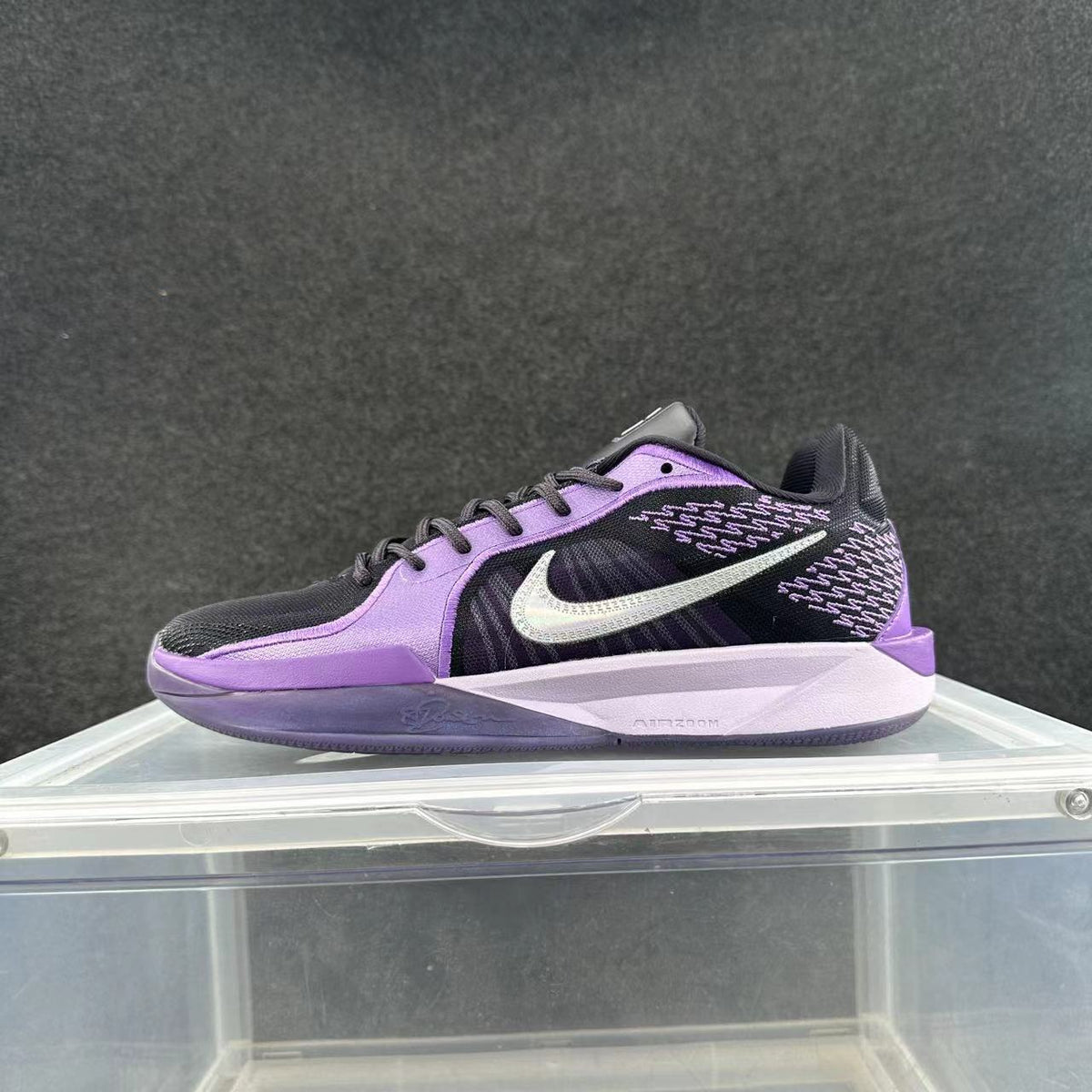 Side view of a purple and black Nike sneaker with a visible Swoosh logo, patterned upper details, and a light-colored Air Zoom-marked midsole.