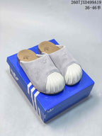 Pair of grey adidas Adimule closed-toe mule slides with white ribbed toe coverings, displayed on a blue shoebox.