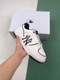 White and black MLB low-top sneaker held in front of its shoebox, showing the side logo, laces, padded collar, perforated toe, and black outsole accents.