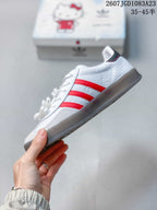 Side view of the white sneaker showing red three-stripe detailing, embossed graphics, and a dark translucent outsole.
