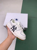 Ivory-white MLB low-top sneaker with a dark navy side emblem, tonal laces, and gum-colored outsole, shown in front of its presentation box.