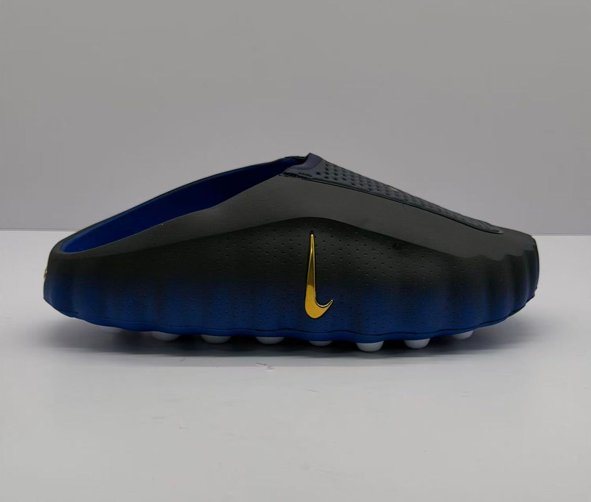 Side view of black and royal blue Nike slides with a gold Swoosh.