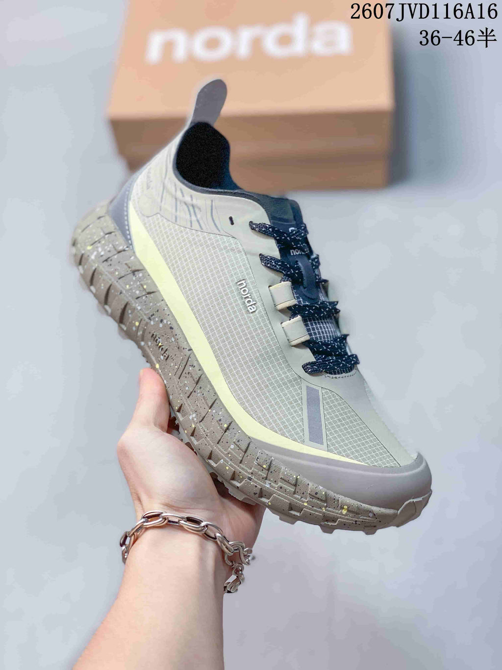 Angled side view of the NORDA shoe showing the light gray upper, dark laces, reflective-looking accents, and thick trail outsole.