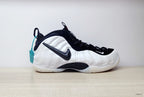 Side view of a white Nike Air Foamposite One sneaker with black Swoosh and dark accents