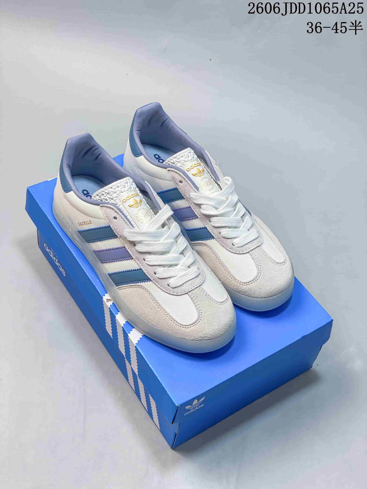 Pair of white adidas Gazelle sneakers with blue and lavender stripes displayed on a blue adidas shoebox.