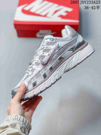 Side profile of a silver and white Nike sneaker showing mesh-look panels, layered overlays, laces, and a ridged midsole; size range 36–42.5 is visible.