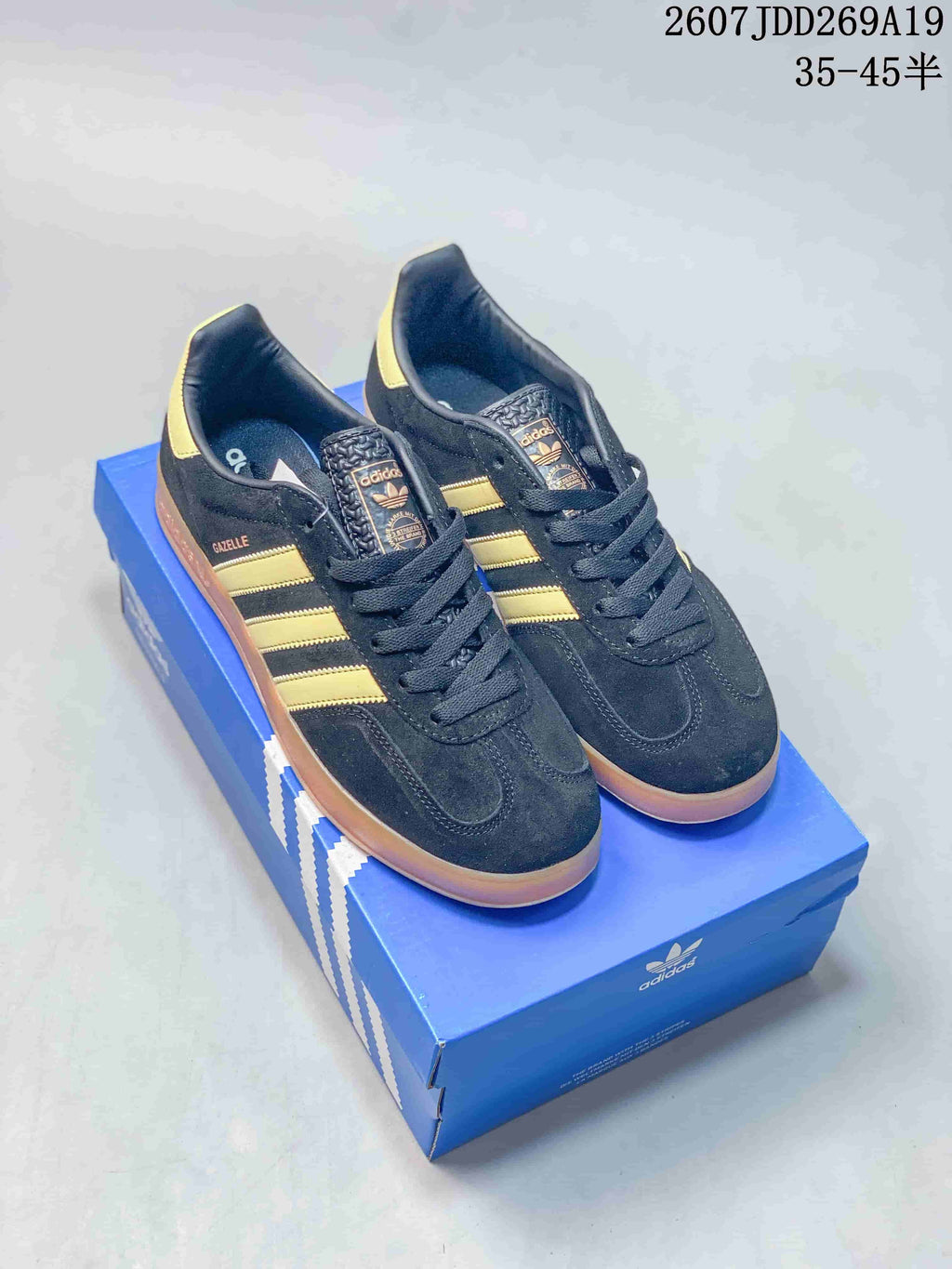 Black Adidas Gazelle sneakers with gold side stripes and gum-colored soles displayed on an Adidas shoe box.