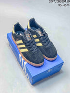 Black Adidas Gazelle sneakers with gold side stripes and gum-colored soles displayed on an Adidas shoe box.