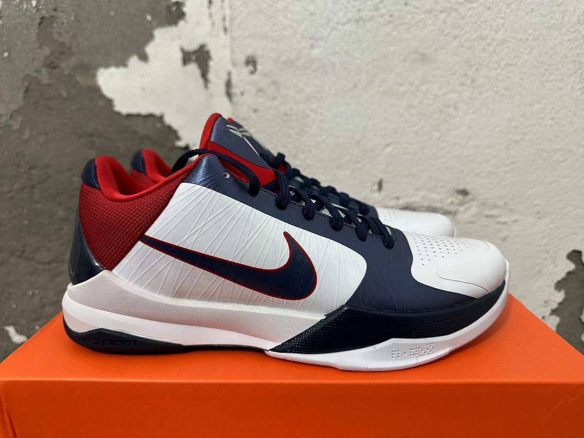 Side view showing the navy Swoosh, white panels, and red heel of a Nike Kobe basketball shoe