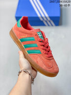 Angled side view showing the visible GAZELLE marking, coral upper, green stripes and gum-colored outsole.