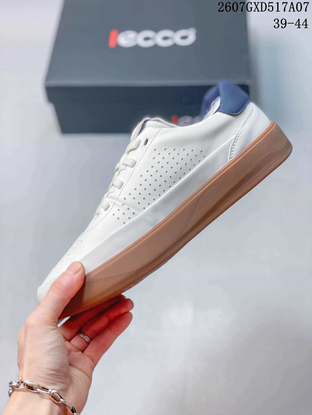 Side view of the white lace-up sneaker showing perforated panels, navy collar detail, and a gum-colored outsole; style code 2607GXD517A07 and size range 39-44 are visible.