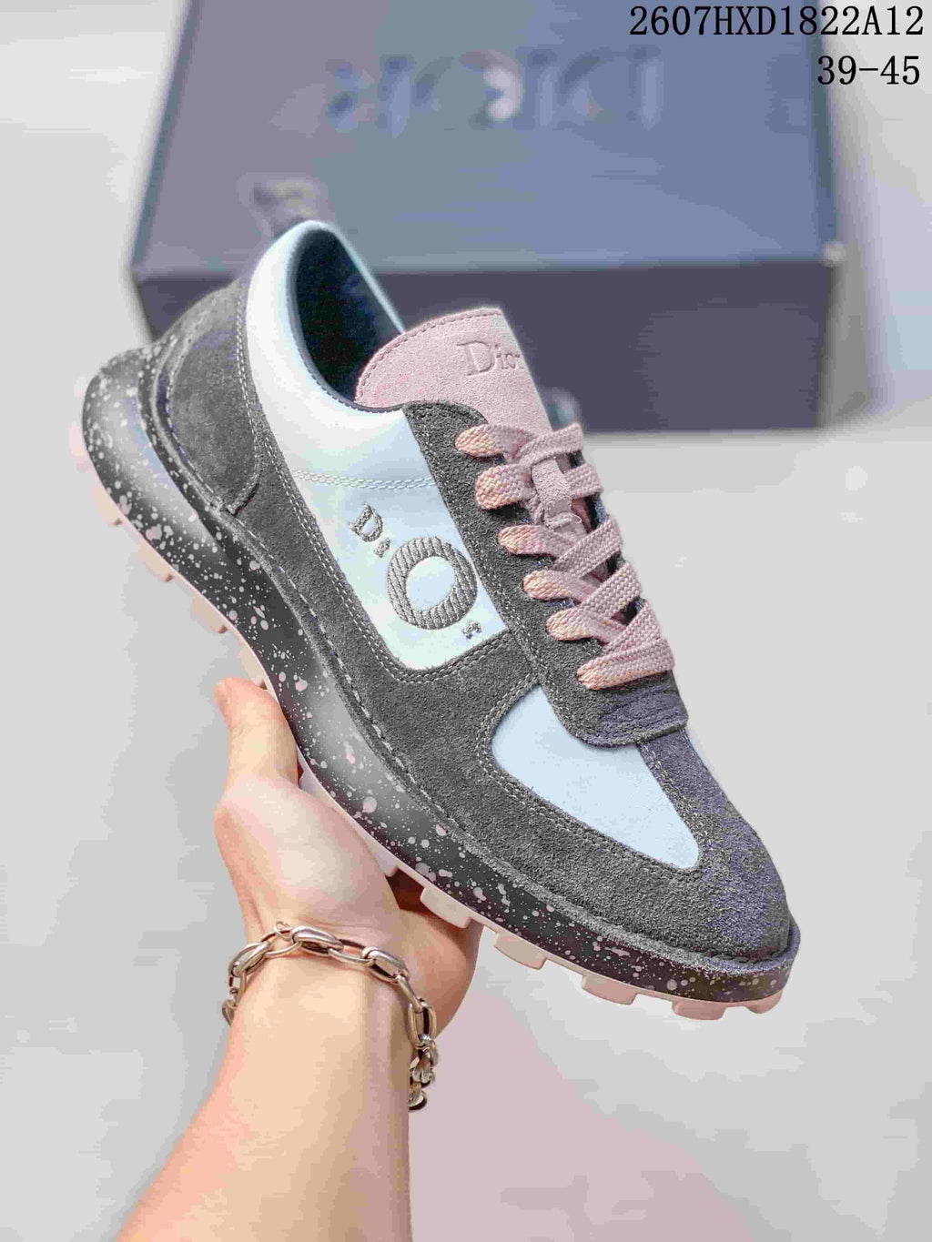 Angled side view of one Dior Squash sneaker showing the gray and white panels, pink laces, side branding, and speckled sole.