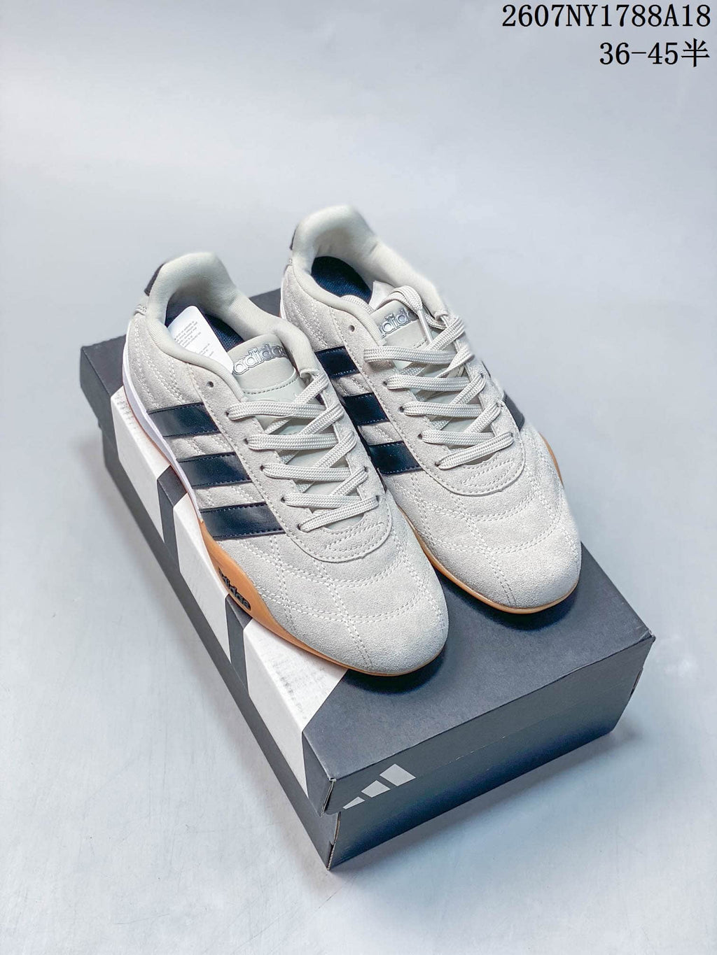 Pair of light-colored adidas Adipista sneakers with dark side stripes and gum outsoles displayed on a shoebox.