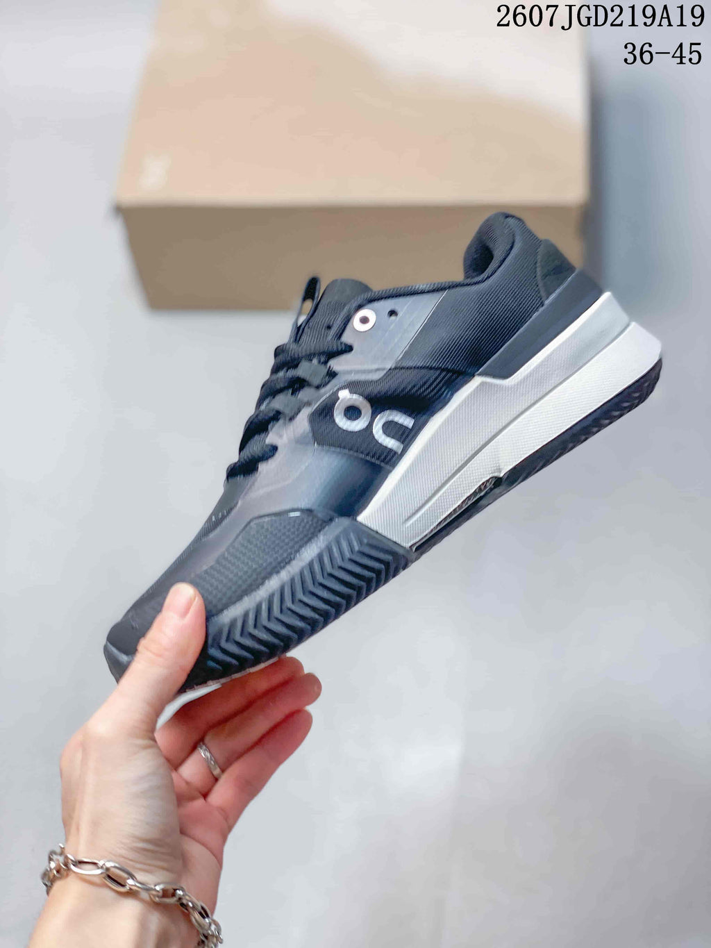 Side view of the black and white low-top tennis shoe showing the layered upper, On branding, contrasting midsole, and patterned outsole; style code 2607TGD219A19 and size range 36-45 are visible.