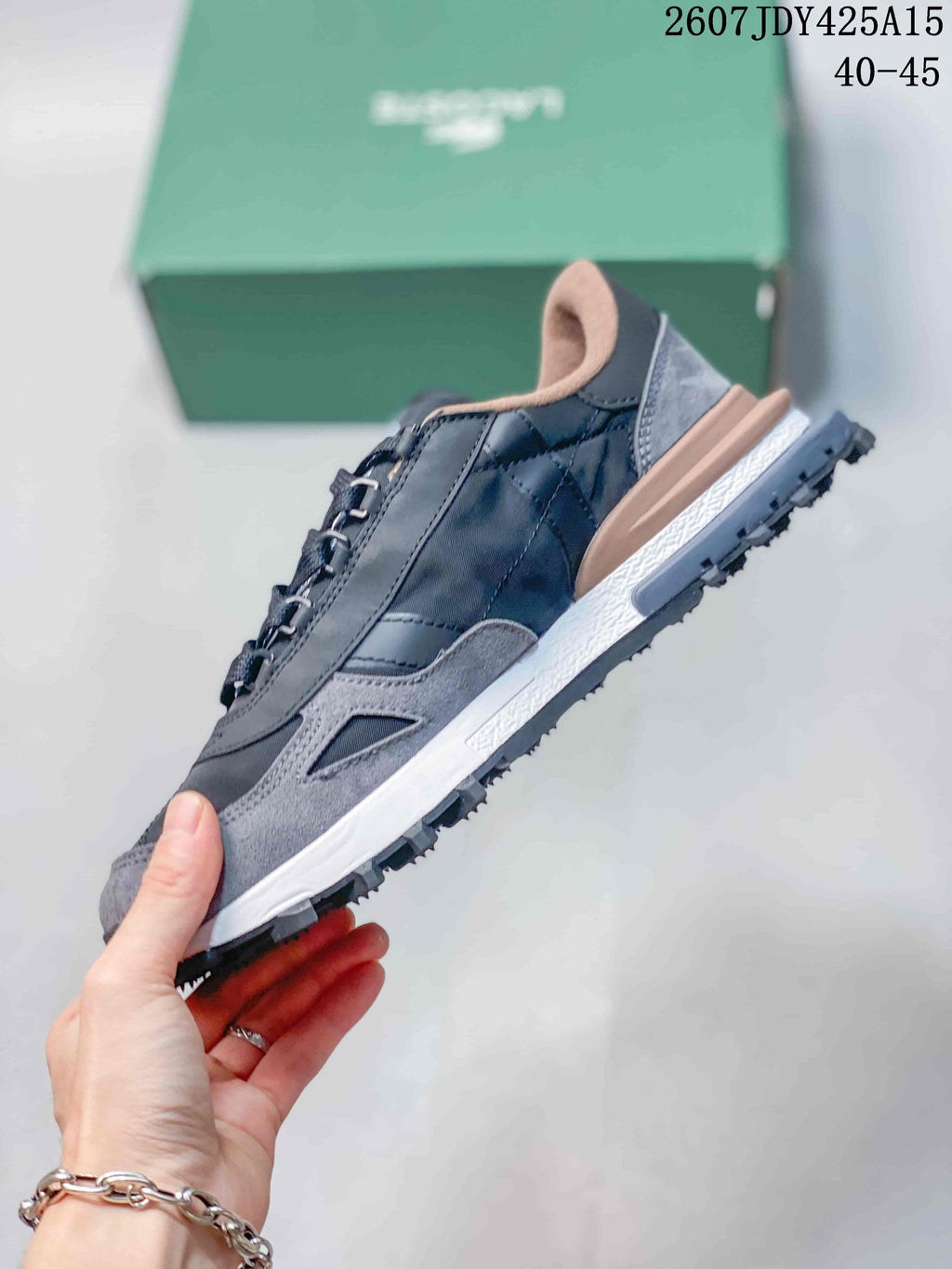 Side profile of a gray Lacoste sneaker showing the layered upper, raised heel section, and textured outsole.