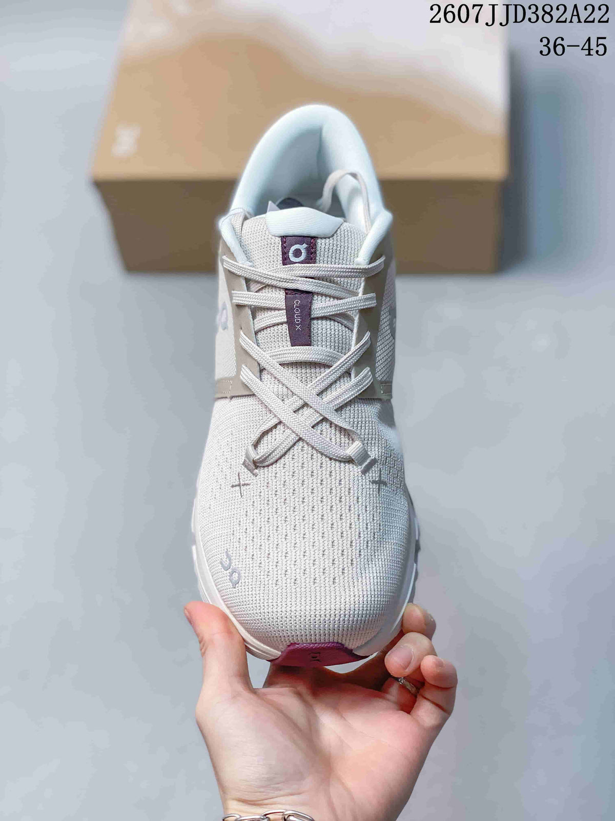 Front view of the light gray lace-up sneaker showing the mesh-style toe box, tongue branding, and burgundy outsole detail.