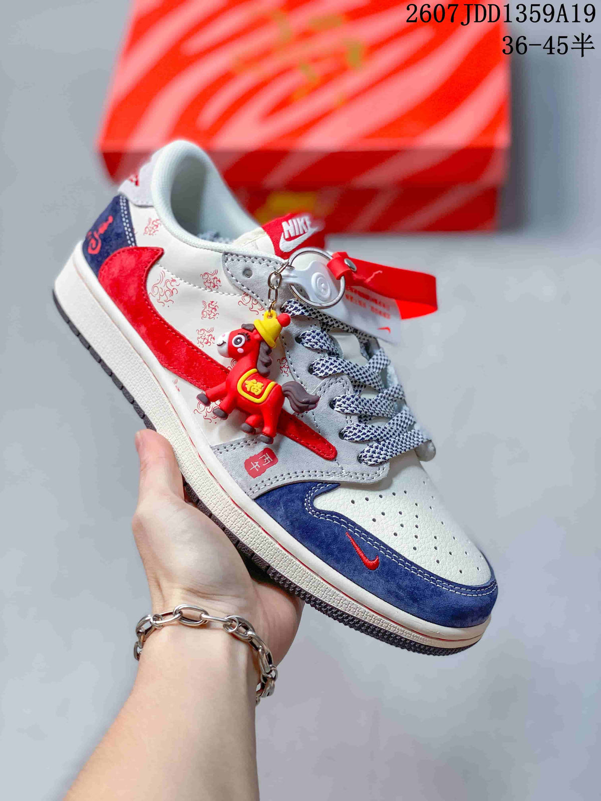 White, red, and navy low-top sneaker with patterned panels, mixed laces, and a decorative hanging charm.