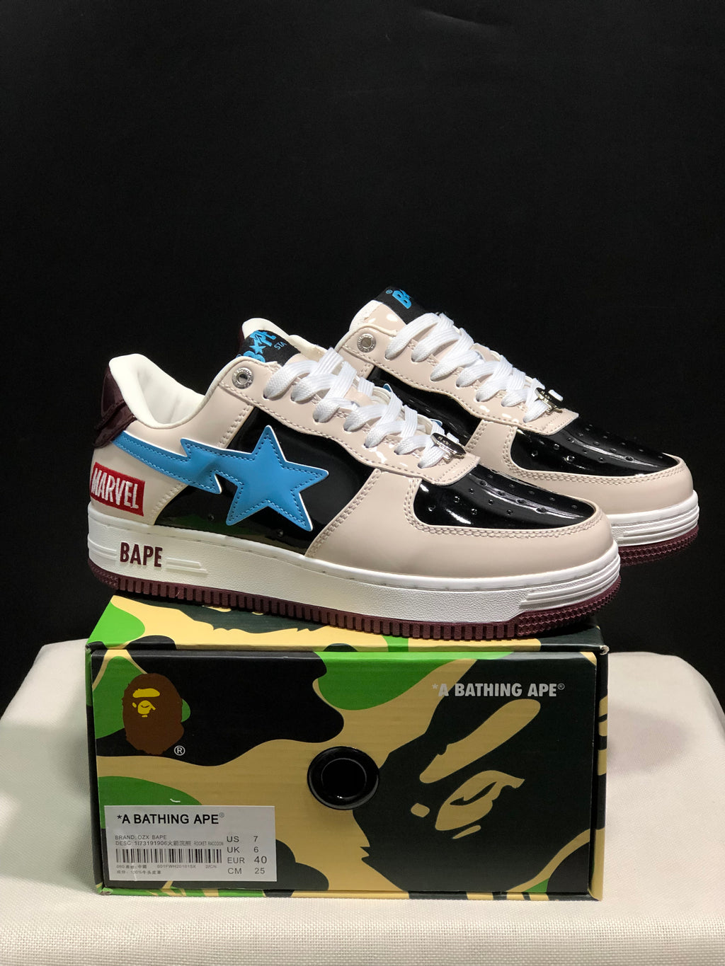 Pair of BAPE Bape Sta low-top sneakers displayed on a camouflage BAPE shoebox, showing cream, black, blue, and burgundy details; the box label shows US 7, UK 6, EU 40, and CM 25.