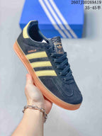 Angled close view of the Gazelle sneaker showing black upper panels, gold stripes, side branding, and gum-colored sole.