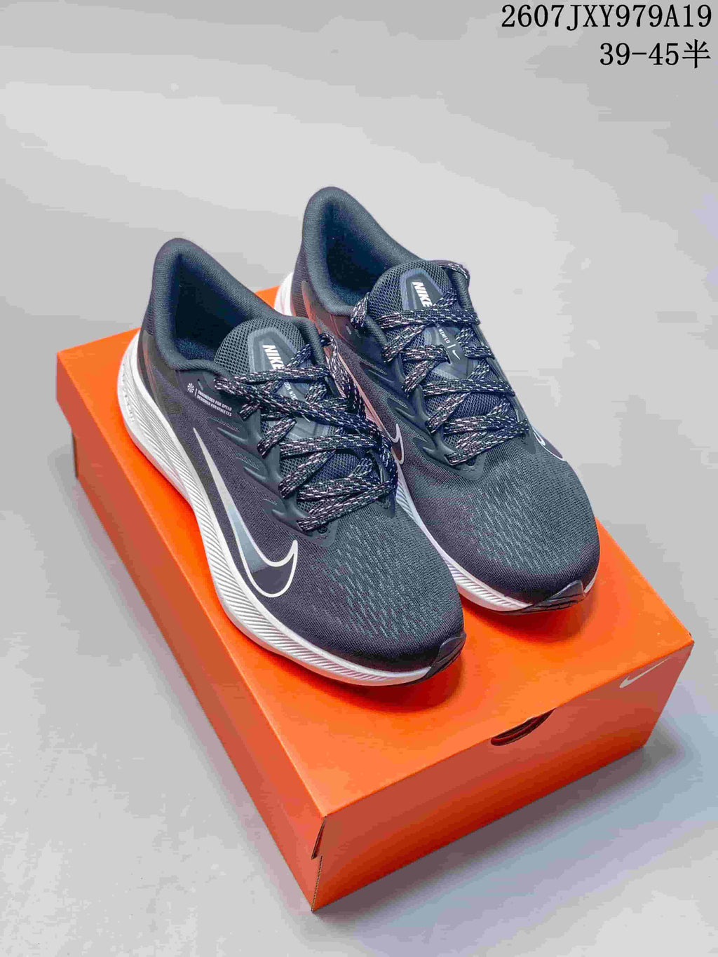 Pair of dark gray and black Nike running shoes with white accents displayed on an orange shoebox.