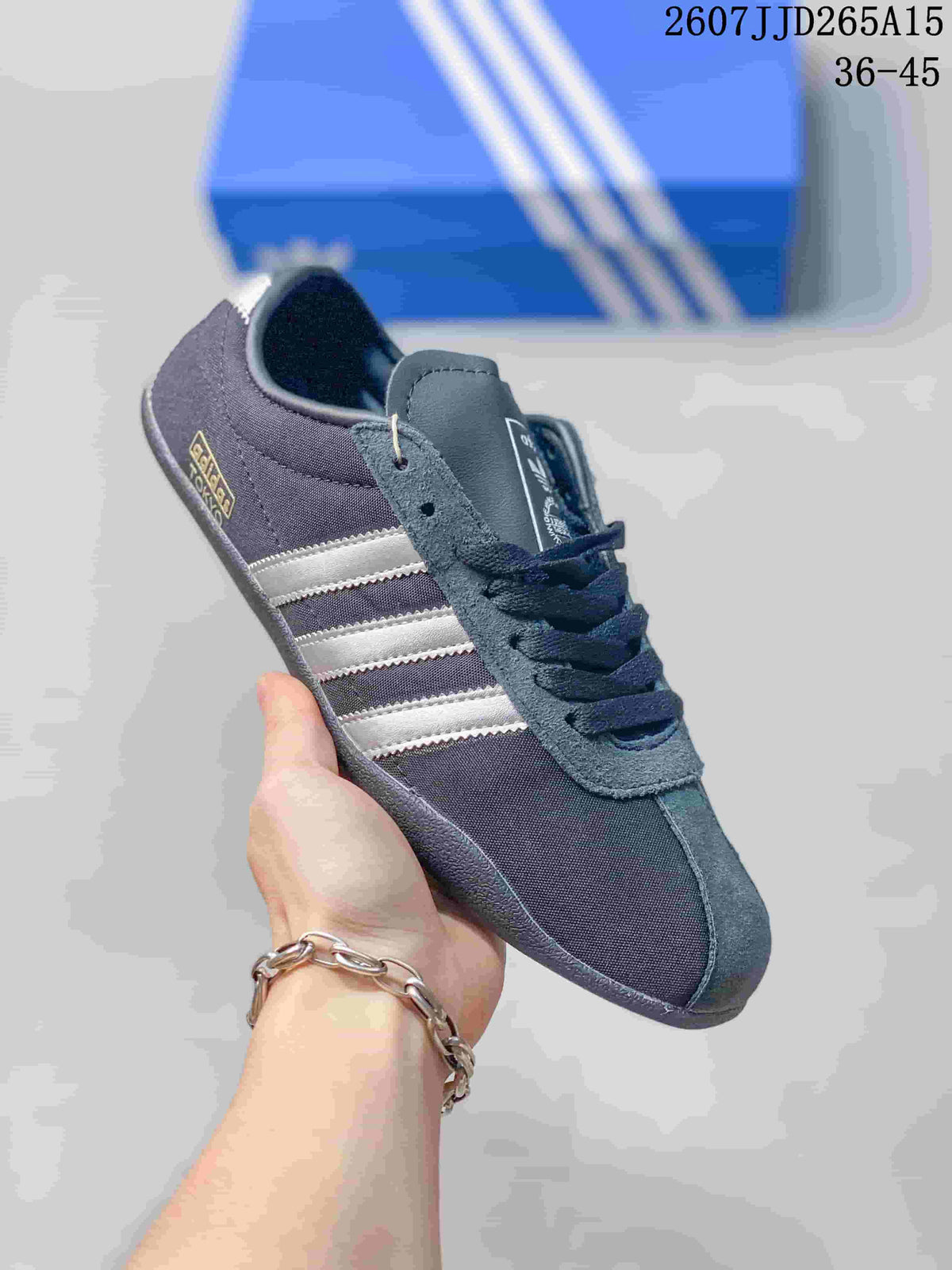 Close-up side view of a black adidas Originals Tokyo sneaker with light gray stripes, dark laces, textured gray overlays, and a dark outsole.