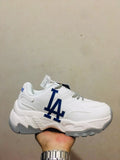 White and gray chunky sneaker with a large blue LA-style side graphic, patterned laces, layered panels, and a textured gray outsole.