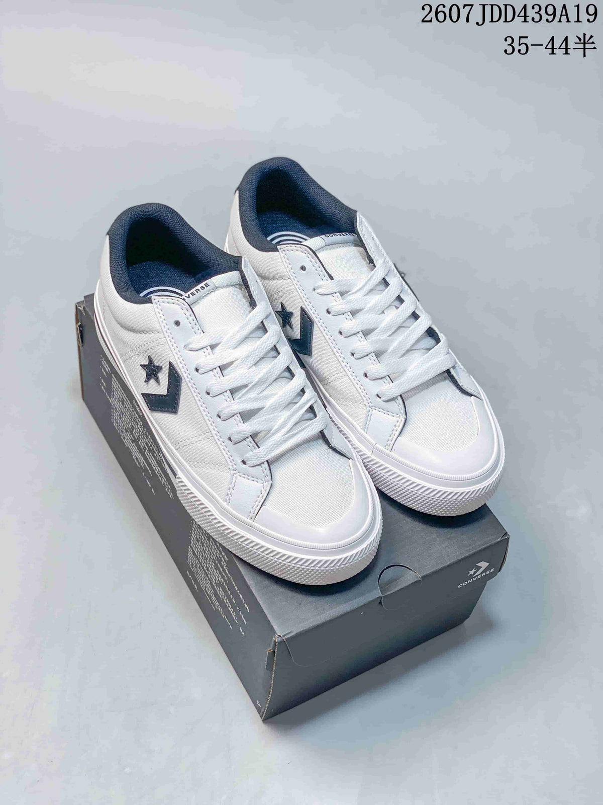 Pair of white Converse All Star low-top sneakers displayed on a branded shoe box, showing dark star-and-chevron side details.