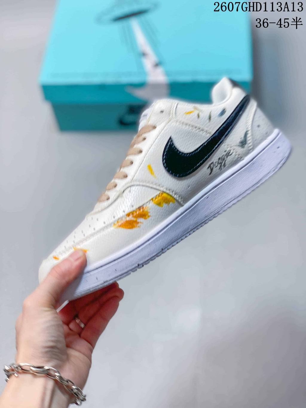 Side profile showing the white low-top sneaker, black Swoosh, beige laces, white midsole, and multicolor graffiti artwork.