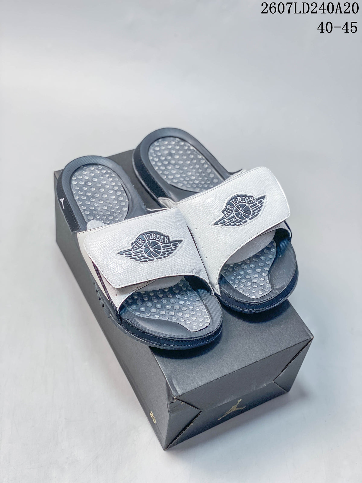 Pair of white and navy Nike Air Jordan slides displayed on a black shoebox; overlay text shows style code 2607LD240A20 and size range 40–45.