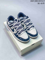 Pair of navy and white Nike SB Dunk Low sneakers displayed on a shoebox, showing layered rope laces and contrasting panels.